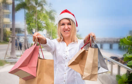 girl in santa hat shopping with many bags. woman walks along the embankmentの写真素材