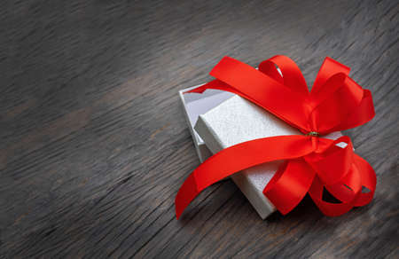 white box with the red bow on the dark brown wooden backgroundの写真素材