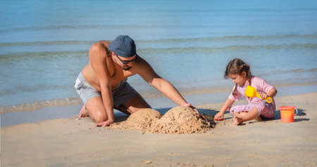 dad and daughter are building the sand castle on the beach. man plays with his daughter by the seaの写真素材