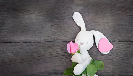 rabbit toy with flower and heart on a wooden background. white hare holding pink rose and heart copy spaceの写真素材