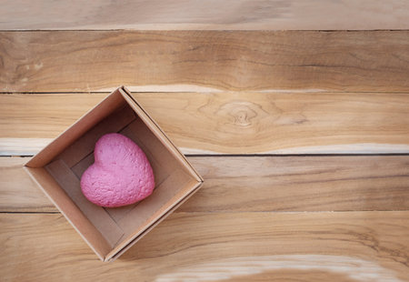 Heart in a gift box on a wooden background. The pink heart is preserved in a cardboard box.の写真素材
