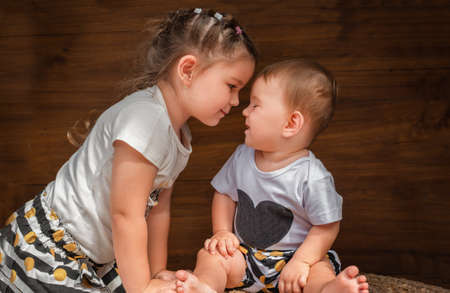 Portrait of sisters on the wooden background. The child wants to kiss the babyの写真素材
