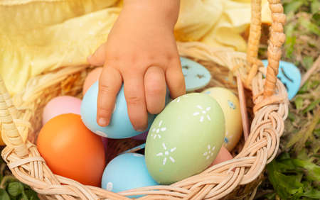 The child's hand takes an Easter egg from the basket. Child with Easter hunt on the grass.