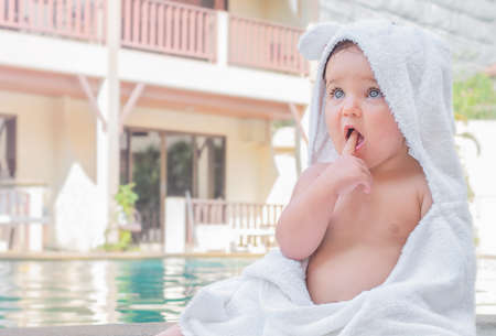 Baby in a towel. The child sits on the side of the pool