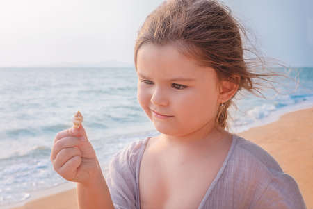 Child examines a seashell on the beach of the seaの写真素材