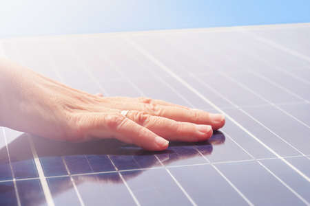 Women's hand on solar panels against the background of the sky.の写真素材