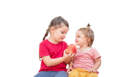 Two children share an apple. A girl holds out an apple to her younger sister.の写真素材