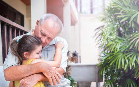 Retired senior with child outdoors. Grandfather hugs granddaughter on a walkの写真素材