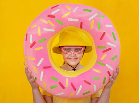 Child on vacation on a yellow background. Girl looking through the circle for swimming
