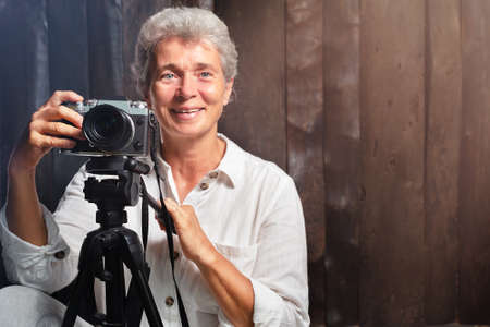 Portrait of elderly woman photographer with camera on wooden backgroundの写真素材