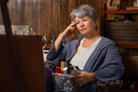 Portrait of a woman artist. The old lady looks at the easel and ponders