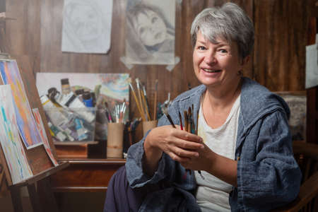 Portrait of the artist with brushes and paintings. Woman is engaged in a hobbyの写真素材