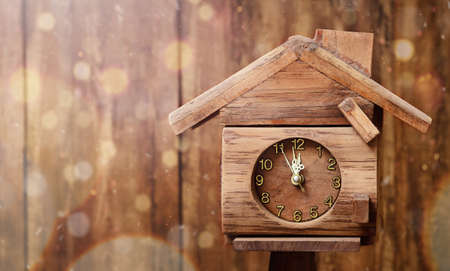 A clock in the form of the house shows midnight on the background of the wooden wallの写真素材