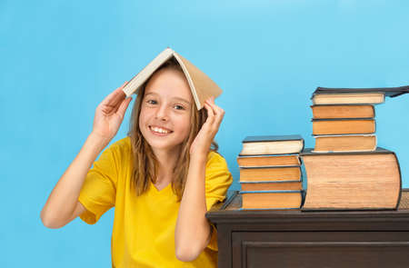 A girl holding a book above her head next to a stack of books on a table on a blue background