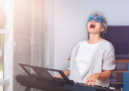 Elderly cheerful woman playing piano, dancing and singingの写真素材