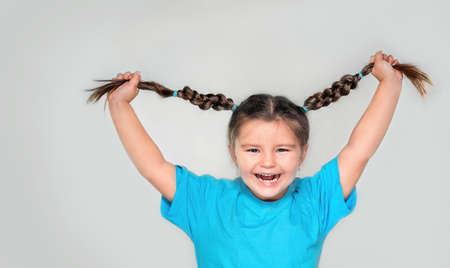 Happy child holding pigtails and laughing on gray backgroundの写真素材