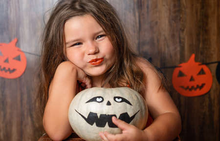 Halloween portrait of child girl with pumpkin on wooden backgroundの写真素材