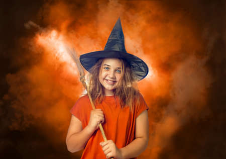 Portrait of the child dressed as the witch with the broomstick stands in the orange smokeの写真素材