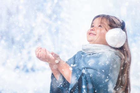 Child girl walks in the winter forest and catches snowflakesの写真素材