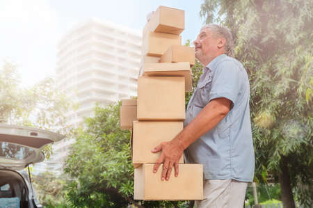 Senior man carries a high stack of cardboard boxes for moving in the carの写真素材