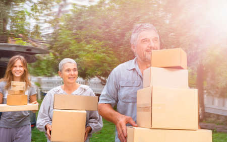 A happy family moves the boxes from the car to their new home. Moving with cardboard boxesの写真素材