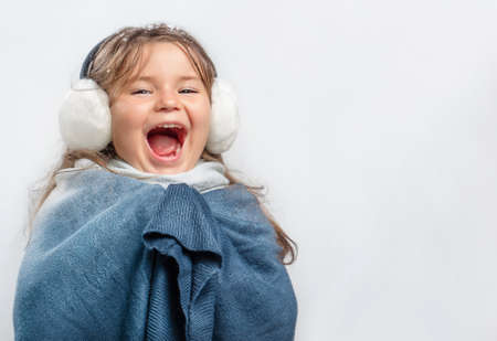 Child girl in earmuff and warm clothes screaming with joy on gray backgroundの写真素材