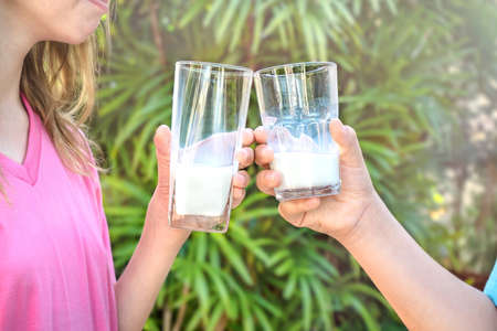 Two children holding glasses with milk on the background of palm treesの写真素材
