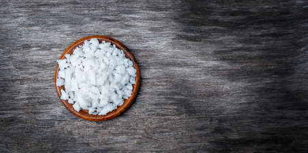 Coarse sea salt in a wooden cup on a wooden surface