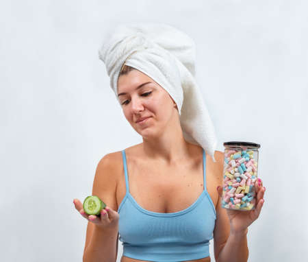Young woman chooses between marshmallows and cucumber on gray backgroundの写真素材