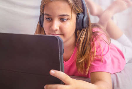 Teenage girl in headphones looking at a tablet on the couchの写真素材