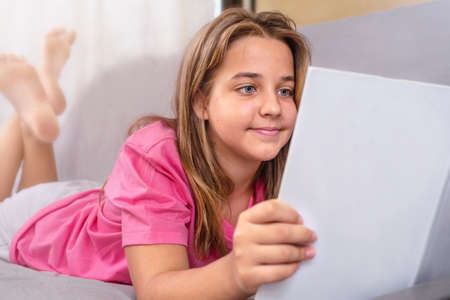 Teenage girl reading a book lying on the couchの写真素材