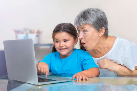 Granddaughter shows something to surprised grandmother in laptopの写真素材