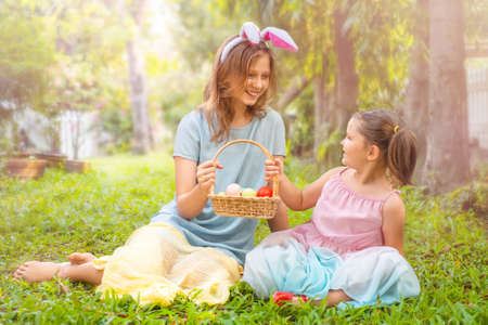 Children sit on the grass and hold a basket with easter eggs in the backyard outdoorの写真素材