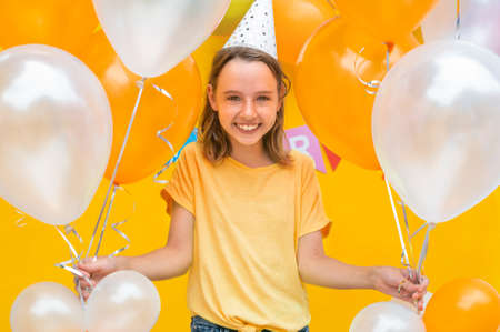 Portrait of the teenage girl with balloons for the birthday party on a yellow backgroundの写真素材