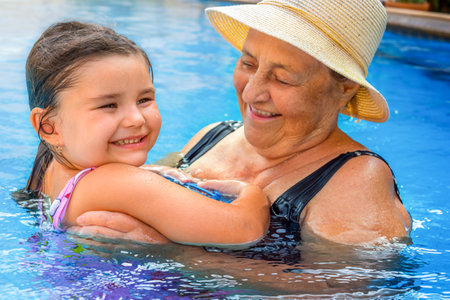 Great-grandmother swims in the pool with a child. Senior hugging a child in the waterの写真素材