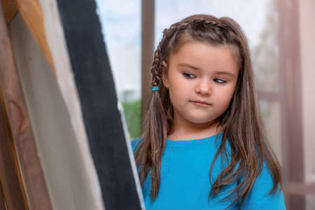 Child girl looks at an easel with a pictureの写真素材
