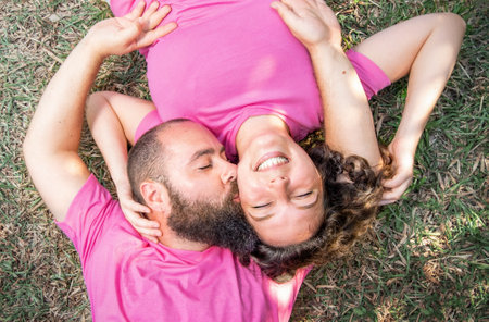 Young family couple lies on the grass and hugs