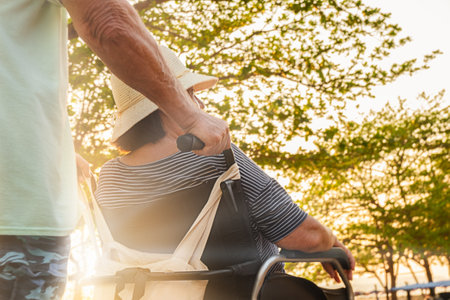 Senior couple on a walk. A man carries his wife in a wheelchair