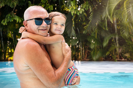 Senior and child hugging in pool on vacation outdoorの写真素材