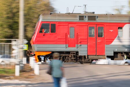 A local train of Russian Railways rushes past people standing at the railway crossing.の写真素材