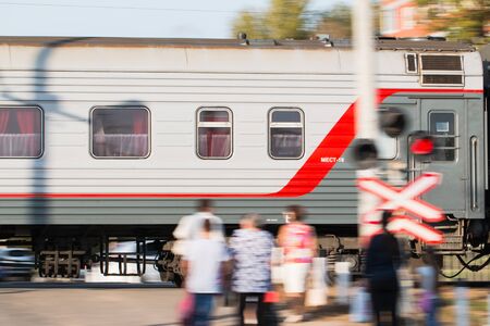 A long-distance train of the Russian Railways rushes past people standing at the railway crossing.