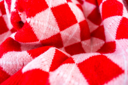 A close-up of a vibrant red and white checkered knitted fabric, showcasing a classic argyleの写真素材