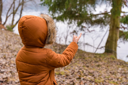 Child in a winter padded coat pointing towards a tree by the river in a Czech Republic forestの写真素材