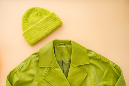Flat lay of green faux leather coat , cashmere hat made from recycled materials on beige backgroundの写真素材