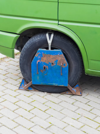 Close-up of a green vans wheel locked with a blue and rusted metal clamp due to illegal parking.