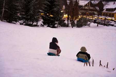 Two people, a child and an adult, sled down a snow-covered hill at dusk