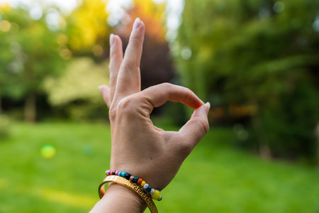 Female hand making an OK gesture with colorful bracelets in a green garden backgroundの写真素材