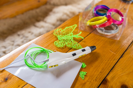 3D printing pen and colorful filaments on wooden table with green butterfly shape, selective focus