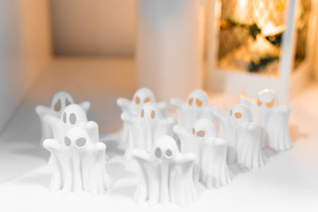Mini white ghost figurines for Halloween decor on white background with warm lightの写真素材