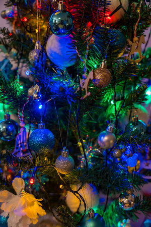 Artificial Christmas tree with blue ornaments and glowing festive lights at home in the dark.